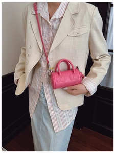 Detail of pink cylindrical bucket bag with embossed bows and adjustable shoulder strap