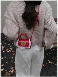 Detail of red patent leather shoulder bag with plush bear and lace trim on a model