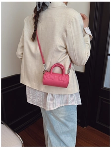 Detail of pink mini cylinder bag with embossed bows and detachable shoulder strap