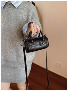 Detail of a black cylindrical crossbody bucket bag with 3D bow relief and slim shoulder strap