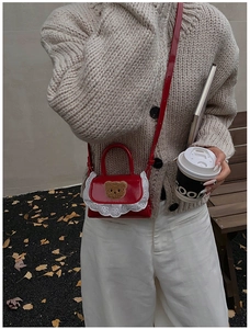 Detail of red faux leather kids handbag with plush bear patch and delicate lace trim