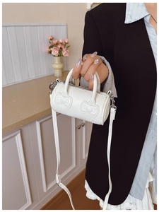 Close-up of a white mini cylinder bucket bag with cute bow detail and silver zipper
