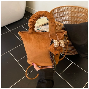 Close-up of brown suede tote bag featuring a teddy bear charm and ruffled handle details
