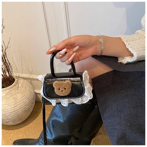 Détail du mini sac à main en cuir noir avec bordure en dentelle et ours en peluche