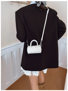 Rear view of a girl carrying a mini cream cylinder bag with cute bow stitching detail