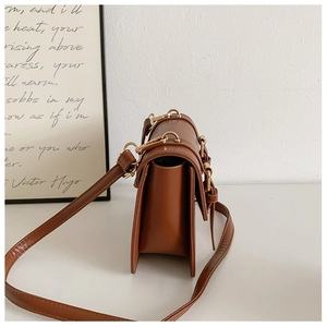 Detailed side view of brown leather crossbody bag with gold metal buckle and gusseted side