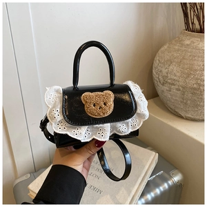 Detail of mini black patent handbag with cute plush bear patch and white lace trim