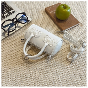 Flat lay of white barrel bag with bows on textured rug with lifestyle accessories