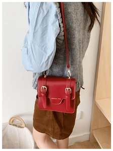 Detail view of a vintage red PU leather crossbody bag with gold metal buckles and flap