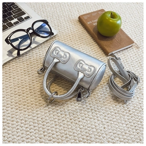 Silver cylinder handbag with a quilted bow detail and adjustable shoulder strap on a rug