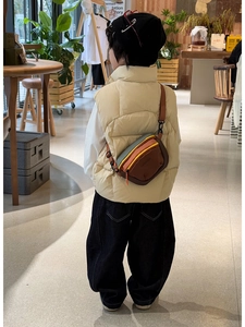 Rear view of a kids colorful patchwork crossbody bag with adjustable brown strap in a cafe