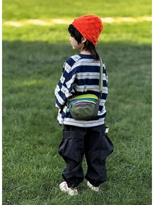 Outdoor view of child wearing a multi-color nylon crossbody bag on a grassy field