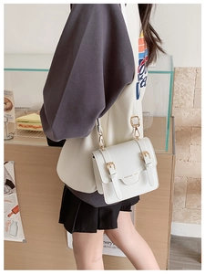 Detail of cream crossbody satchel with gold buckles and fashion text in a cafe setting