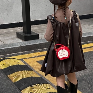 Outdoor view of a small red round cartoon rabbit crossbody bag with a gold chain strap