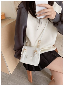 White vintage style kids messenger bag with gold buckles worn in a warm indoor setting