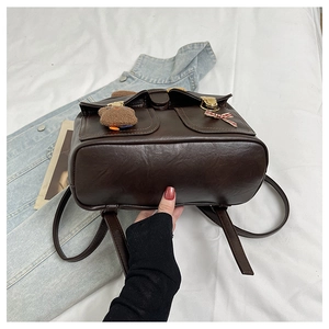 Detail view of brown faux leather backpack base with cute plush bear and bow charm