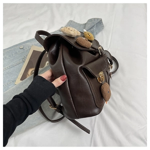 Close-up of brown leopard print backpack with plush charms and magnetic side pocket