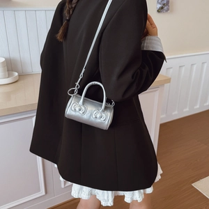 Silver mini cylinder bucket bag with bow details worn by a girl in a black suit