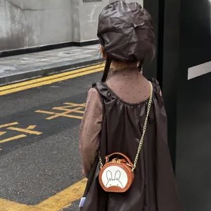 Rear view of a child wearing a brown round crossbody bag with a cute rabbit and metal chain