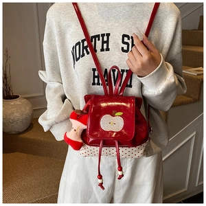 Detail of red apple backpack with polka dot trim and plush apple charm on a small model