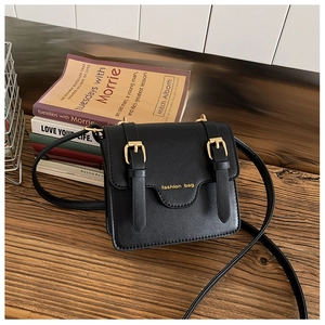 Detail of black faux leather messenger bag with gold buckles on a wooden desk
