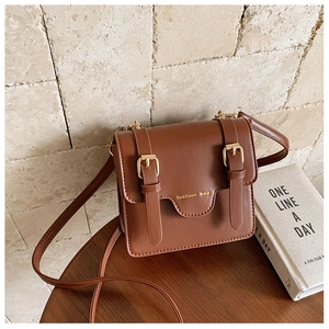 Detail of vintage brown leather crossbody bag with buckle straps and golden fashion bag text