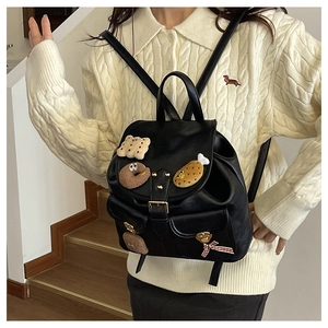 Detail of black glossy PU backpack with cute plush doll pins and red plaid bow decoration