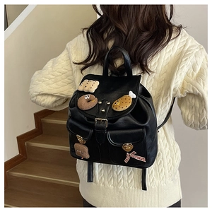 Detailed back view of a black plush kid backpack with cute patches on a wooden staircase