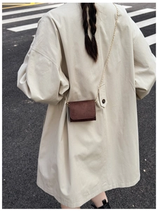 Braune Mini-Umhängetasche aus mattem Wildleder mit goldener Kette über einem Trenchcoat