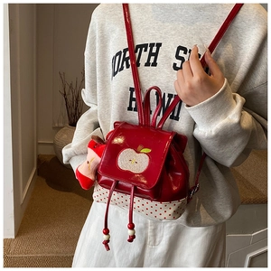 Detail view of kids apple backpack showing polka dots and apple plush pendant