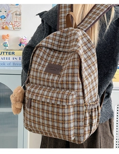 Detail view of British style plaid backpack featuring a plush bear charm and mini bag label