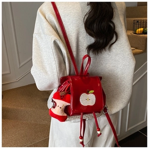 Close-up of red apple-themed kids backpack with plush charm and polka dot accents
