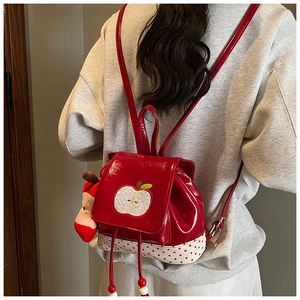 Detail of red apple backpack with polka dots and plush charm on white background