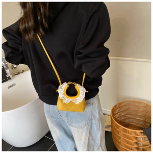 Detail of yellow suede mini bag with white lace trim worn over a black hoodie
