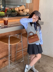 Close-up of child modeling a brown leather mini tote bag with stripe shirt and knit vest