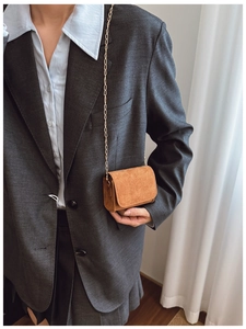 Nahaufnahme der braunen Wildleder-Minikette-Tasche mit Goldkette auf grauem Sakko