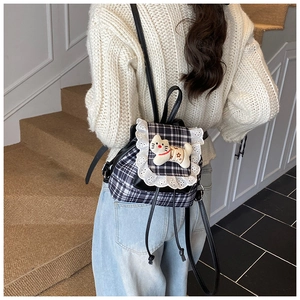 Detail of cute cat plush and lace trim on plaid backpack for girls in indoor setting