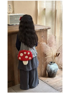 Détail d'un sac bandoulière en peluche champignon porté par un enfant dans un décor cosy