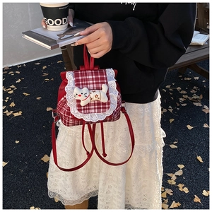 Detail of red plaid backpack with delicate lace trim and a cute plush cat doll