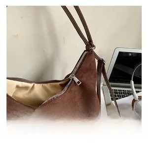 Détail du sac hobo en daim marron foncé avec fermeture éclair argentée dans un bureau chic