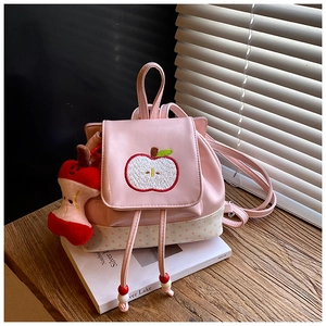 Detail of pink polka dot kids backpack featuring apple embroidery and plush apple charm