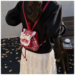 Outdoor shot of a red plaid toddler backpack with lace trim and a cute plush kitten charm
