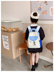 Detail view of lightweight color-block children backpack on a model in a bakery setting