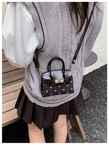 Detailed side view of a black polka dot mini handbag with a gold-tone clasp on a model