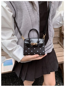 Detailed view of mini polka dot handbag with gold lock and black leather crossbody strap