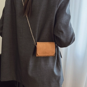 Mini-Umhängetasche aus braunem Wildleder mit Goldkette für Kinder auf grauem Blazer