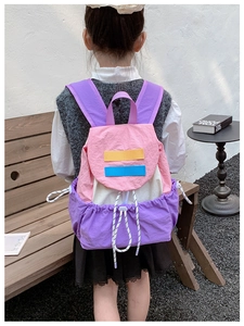 Outdoor back view of a colorful pink and purple color-block kids backpack with drawstrings