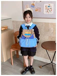 Kids color-block backpack with drawstring closure shown in a cozy indoor lifestyle setting