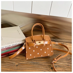 Close-up of a mini brown polka dot handbag with suede texture and gold turn-lock closure