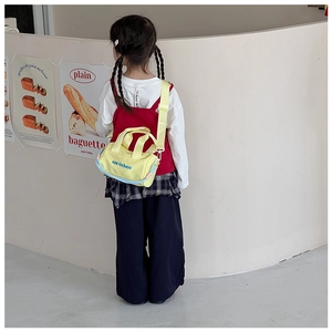 Detail of yellow nylon cylinder kids bag with turquoise letter print and blue base trim